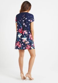 Kratší rukávy, áčková šaty z navy látky s živým květinovým potiskem v růžové, bílé a zelené. Hladký povrch s skrytým zipem vzadu.