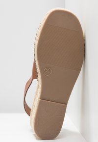 Sandale marron avec une semelle intermédiaire en jute tissé, une semelle en caoutchouc et un talon plat. Taille 37 imprimée au bas. Texture lisse avec un minimum de détails.