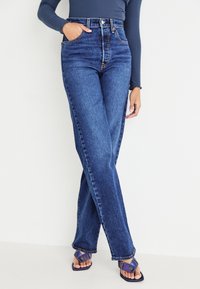 Blå jeans i hög midja med raka ben, utrustade med fickor och subtila sömmar, kombinerade med lila klackskor.