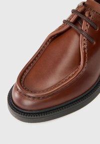 Braunes Leder-Schuhwerk mit runder Zehenpartie, harmonischer Naht und einer schwarzen strukturierten Sohle mit einer dekorativen Kante um den Rand.
