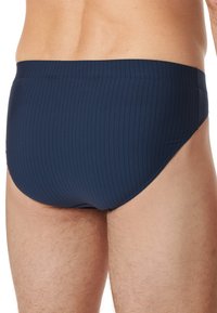 Tmavě modré plavky s vertikálním žebrováním, elastickým pasem a hladkým materiálem; navrženy pro těsné obepnutí a minimální zakrytí.