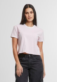 Lyserød kort t-shirt med korte ærmer, hvid rund halsudskæring og ærmekanter, lavet af blødt bomuldsstof. Kombineret med mørke jeans.