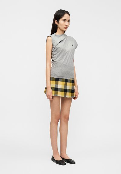 Γκρι εφαρμοστό τοπ με ασύμμετρο σχεδιασμ ό ώμου, συνδυασμένο με κίτρινη και μαύρη μίνι φούστα καρό. Μαύρα μπαλέτα ολοκληρώνουν την εμφάνιση.