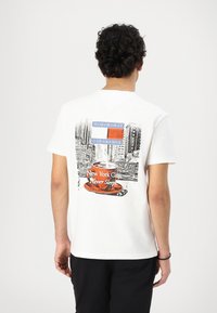 White cotton t-shirt featuring a graphic design of a coffee cup with "New York City Never Sleeps" text and cityscape illustrations on the back.