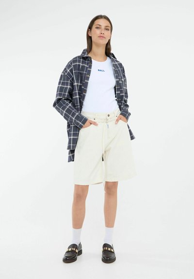 Camisa de franela a rayas navy sobre una camiseta blanca, pantalones cortos crema, calcetines blancos y mocasines negros con detalles dorados. Estilo casual, corte relajado.