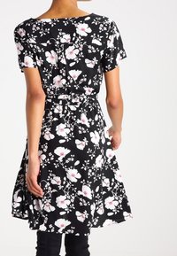 Vestito nero a fiori con maniche corte, vita cincata e gonna ampia. Il design presenta motivi floreali bianchi e rosa.