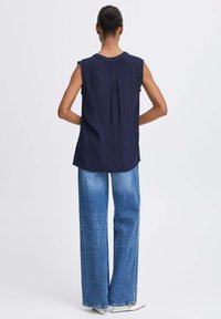 Top sans manches bleu marine avec une texture unie et un détail de plis au dos, associé à un jean en denim bleu clair taille haute.