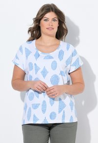 Camiseta blanca con patrones geométricos azules, cuello redondo y mangas cortas, combinada con pantalones grises. Tejido de algodón ligero.