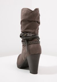 Bota gris de ante con diseño arrugado, correa de cuero negra con orificios y tacón alto negro. Detalle notable de costura en la bota.