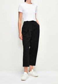 Pantalons rayés noir et blanc avec une coupe décontractée, dotés de poches latérales et d'une taille haute, associés à un t-shirt blanc uni et des baskets blanches.