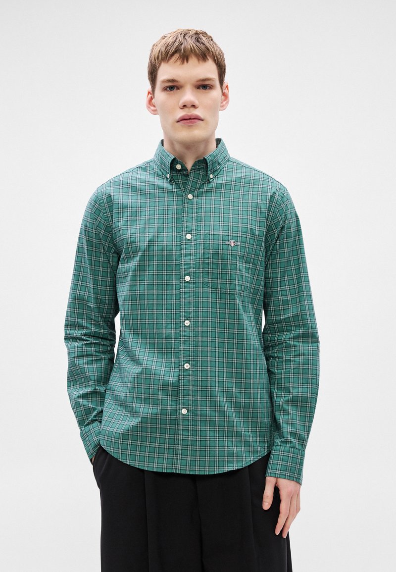 Green plaid button-up shirt with a collar, featuring white buttons and a small logo on the chest. Smooth cotton fabric, classic fit.