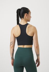 Čierny športový crop top s dizajnom pretekárského chrbta, kombinovaný s vysokými zelenými legínami, ktoré majú textúrovanú tkaninu a viditeľné švy.