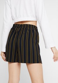 Pantalones cortos a rayas negros y amarillos con una cinturilla elástica, que presentan un corte holgado y una textura suave, combinados con una camiseta corta blanca.