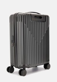 Valigia rigida di colore grigio scuro, dotata di scanalature verticali, serratura combinazione integrata e quattro ruote nere per la mobilità.