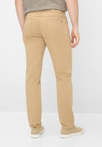 Beige katoenen chino's met een rechte pijp, voorzien van achterzakken en minimale stikseldetails, gecombineerd met beige sneakers.