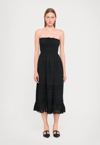 Vestido preto sem mangas com corpete franzido, saia em camadas e acabamentos em renda na bainha. Tecido suave com uma silhueta fluida.