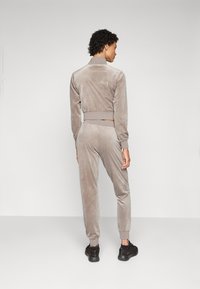Plysj matchende sett i lys beige, med en kort jakke med ribbet midje og matchende smale bukser. Sorte treningssko inkludert.