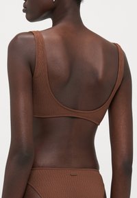 Brown textured bikini with a scoop back design, featuring wide straps and a seamless finish, highlighting a smooth fabric texture.