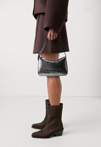 Metallic black handbag with a curved shape, featuring a zip closure and shoulder strap. Logo "Karl Lagerfeld Jeans" embossed on the front.