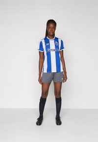 Futbalový dres FC Porto s modro-bielymi pruhmi, s krátkymi rukávmi, so zladenými šedými šortkami, čiernymi ponožkami a čiernymi kopačkami.