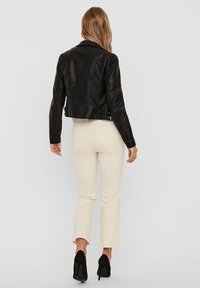 Giubbotto cropped in pelle nera con maniche testurizzate, abbinato a jeans svasati bianco sporco e scarpe con tacco nere.
