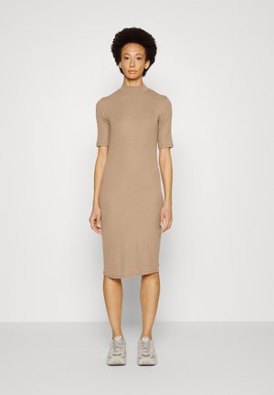 Vestido de malha, de comprimento midi, em bege claro com decote alto e mangas curtas. Usado com ténis cinza claro. Textura suave, design ajustado.