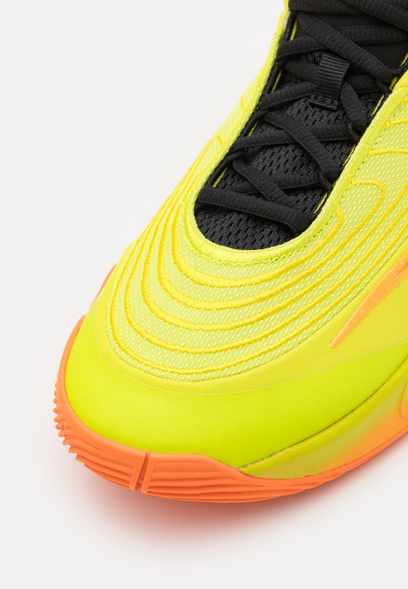 Scarpa atletica gialla fluo con superficie testurizzata, linguetta in rete nera e suola arancione. Presenta un design a strati e dettagli di cucitura prominenti.