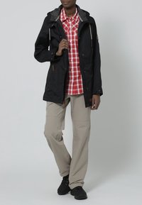 Black waterproof jacket with gray lining, front pockets, paired with a red and white checkered shirt and beige pants, finished with black shoes.