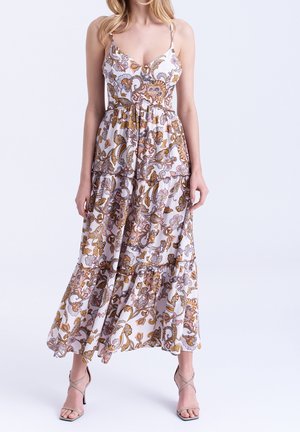 Donna che indossa un vestito lungo bianco senza maniche con motivo floreale paisley marrone e viola e sandali beige con tacco.