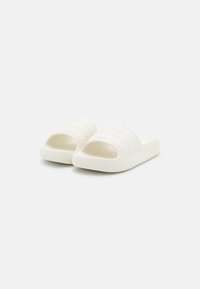 Vita glid sandals gjorda av mjukt material, med en texturerad rem med horisontella utsmyckningar och en öppen tådesign.