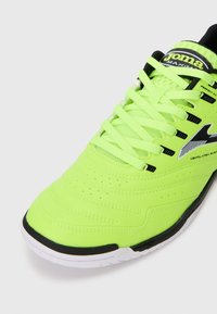 Neon grønn atletisk sko med et strømlinjeformet design, teksturert syntetisk overdel, svarte detaljer og en hvit gummisåle med ventilasjonsdetaljer.