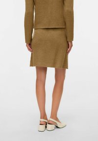 Pruunist kudumist kaheosaline komplekt, mis sisaldab istuvat pikka varrukaga pluusi ja põlveni ulatuvat seelikut. Sobitatud heledate toonidega plokk-kontsaga kingadega.