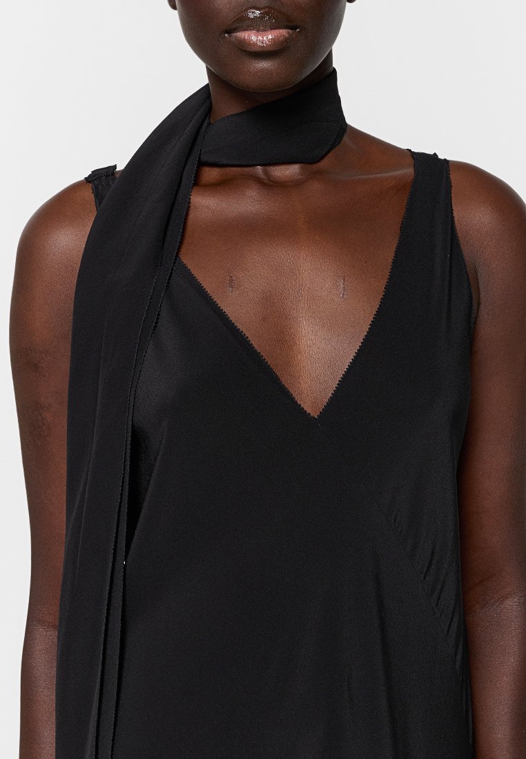 Czarna sukienka bez rękawów z głębokim dekoltem w serek, gładki materiał oraz cienki, dopasowany szalik związany wokół szyi.