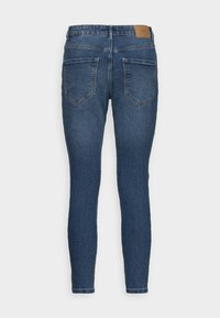 Smal blå denimjeans med en slät textur, fem fickor och en tan läderlapp vid bakre midjan. Klassisk design och åtsittande form.