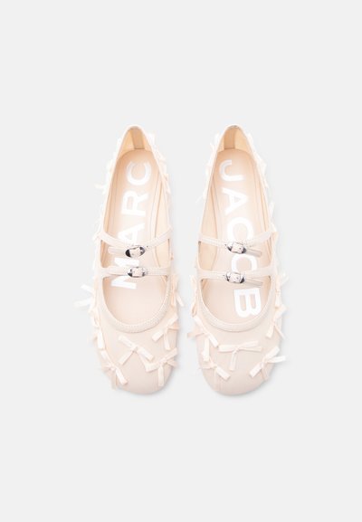 Κρεμ χρώματος μπαλαρίνες με διπλές λουρίδες με αγκράφες και πολλούς μικρούς διακοσμητικούς φιόγκους σε απλό ανοιχτό φόντο.