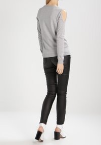 Grå långärmad tröja med axelsnitt, kombinerad med svarta tajta byxor. Modellen har på sig vita klackskor med blockklack. Slät textur, avslappnad design.