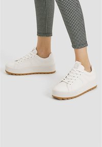 Baskets blanches avec une tige en cuir texturé, une semelle en caoutchouc gomme plate et un bout rond. Lacets et col rembourré pour un ajustement sécurisé.