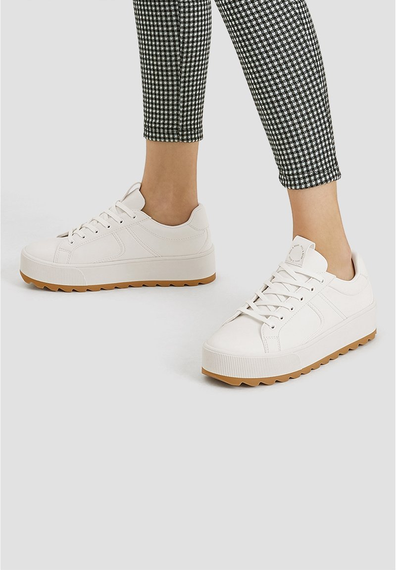 Baskets blanches avec une tige en cuir texturé, une semelle en caoutchouc gomme plate et un bout rond. Lacets et col rembourré pour un ajustement sécurisé.