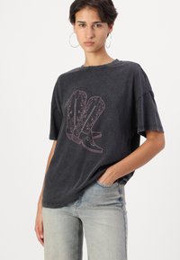 Zwarte oversized t-shirt met een voorzijde graphic van cowboylaarzen met roze details. Zacht materiaal met een relaxte pasvorm en korte mouwen.