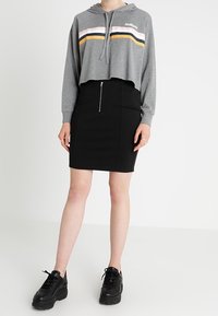 Grå kortärmad hoodie med horisontella ränder i rosa, gult och marinblått, nedan en svart dragkedja blyertskjol och svarta platåsnickers.