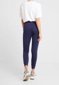 Mörkblå kroppsnära leggings i mjukt material, som smalnar av vid ankeln, i kombination med en lös vit t-shirt och avslappnade sneakers.