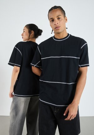 Svart T-skjorte med grå horisontale striper, rund halslinning og korte ermer. Modellen har den på sammen med baggy jeans. Glatt tekstur.