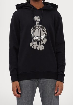 Black hoodie with front graphic of Garfield cat walking, worn by person with gray jeans against plain background.