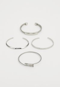 Patru brățări din silver: un cuf neted, un design texturat în formă de cablu, o plăcuță plată cu gravură și un band subțire cu accente numerice.