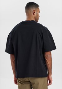 Sort oversized t-shirt lavet af bomuld, med rund halsudskæring og korte ærmer, med en glat tekstur. Vist fra ryggen.
