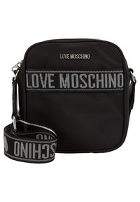 Černá crossbody taška se stříbrnými logy "LOVE MOSCHINO" a nastavitelného tkaného popruhu, na kterém je velkými písmeny vypsáno jméno značky.
