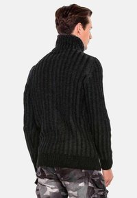 Schwarzer, gerippter Strickpullover mit hohem Kragen und enganliegenden Bündchen, der ein strukturiertes Muster aufweist und am Saum eine lockere Passform hat.