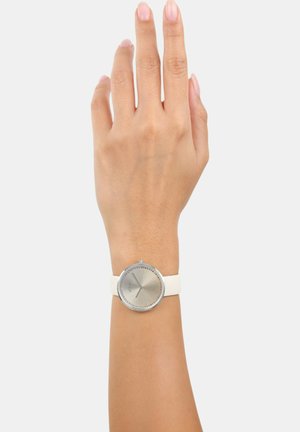 Zilveren ronde horloge met een gestructureerde zilveren wijzerplaat, wit siliconen band, tentoongesteld op een hand tegen een neutrale achtergrond.