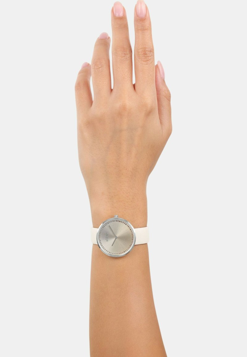 Silberne runde Uhr mit einem strukturierten silbernen Zifferblatt, weißem Silikonarmband, auf einer Hand vor einem neutralen Hintergrund präsentiert.