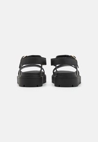 Sorte sandaler med en kraftig gummisåle, med doble brede stropper og et gullspenne, som fremhever et minimalistisk design.
